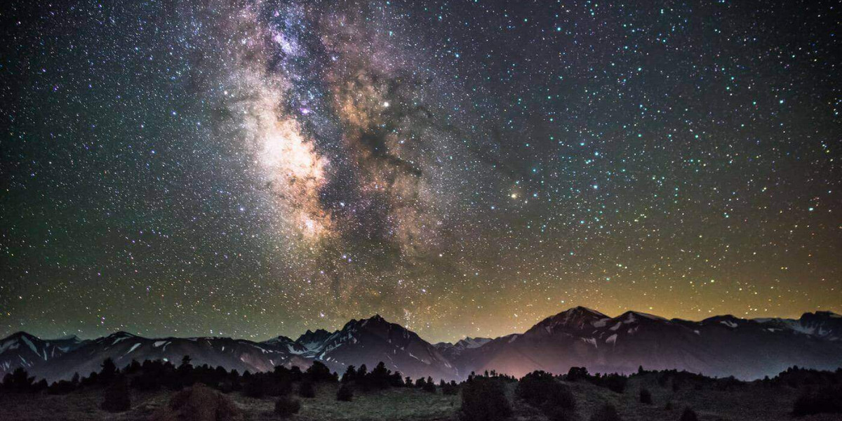 The milky way above a foggy landscape with mountains in the background and a forest in the foreground.